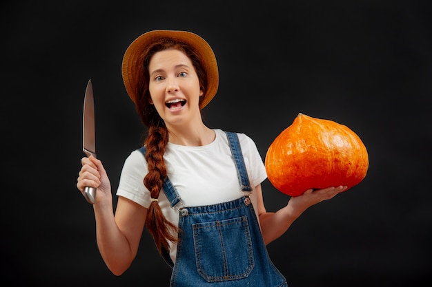 Bäuerin auf schwarzem Hintergrund hält einen Kürbis mit einem Messer zum Schnitzen einer Laterne für Halloween