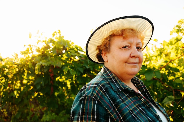 Bäuerin, die lächelt und in die Kamera schaut, hat Hut auf dem Kopf und ist glücklicher Winzer in ihrem Weinberg