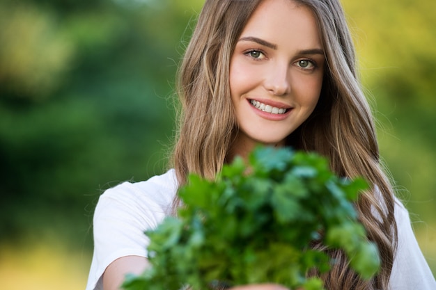 Foto bäuerin hält frisches gemüse angebaut. bauernhofernte. junge frau, die einen bund petersilie hält.