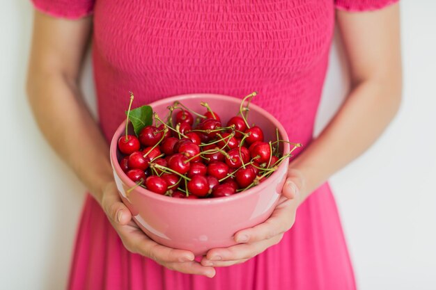 Bagas de cereja closeup em uma tigela rosa nas mãos femininas