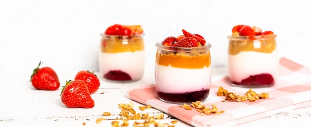 Bagas de iogurte de frutas com muesli e morangos frescos, em um fundo branco de madeira, saudável