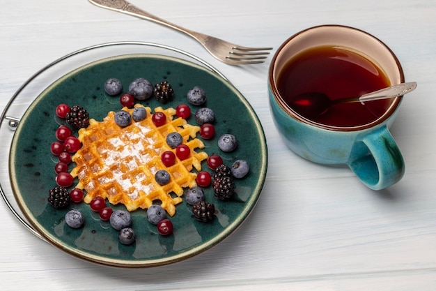 Bagas e waffles em um prato azul Uma xícara de chá e um garfo na mesa