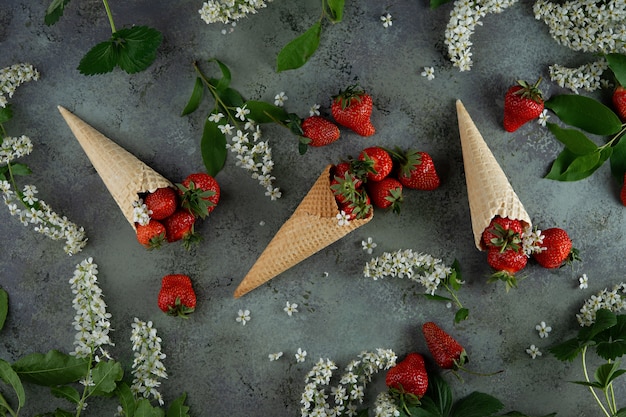 Bagas frescas da morango em cones do waffle e flores e ramos da cereja de pássaro.