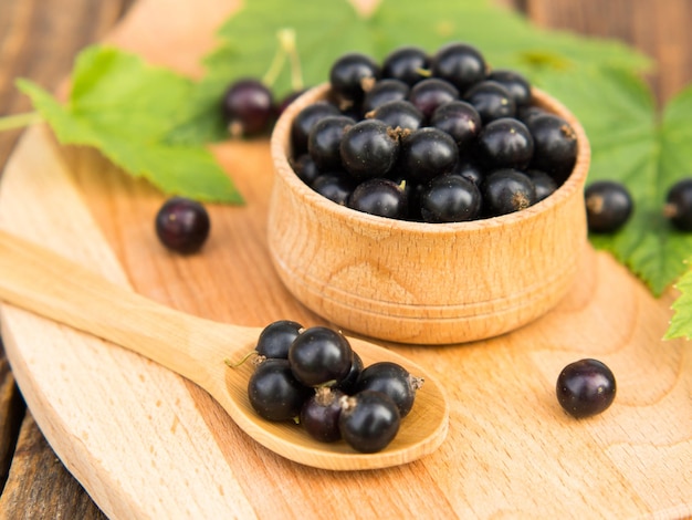 Bagas frescas de groselha preta em uma tigela sobre uma mesa de madeira perto de folhas verdes Frutas suculentas de groselha natural Groselha preta