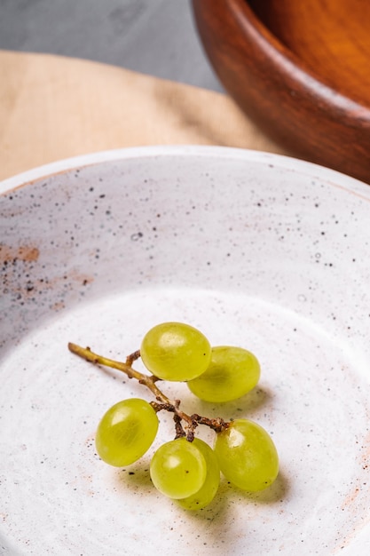 Foto bagas frescas de uvas brancas maduras em uma tigela de madeira com um prato na toalha de mesa de linho, concreto de pedra, macro de visão de ângulo