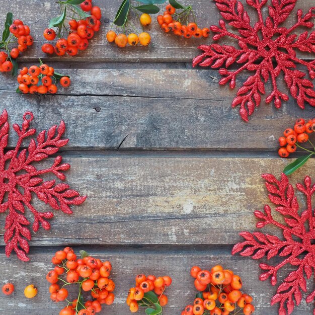 Bagas vermelhas laranja e amarelas de inverno Rowan em um fundo horizontal de madeira Flocos de neve grandes e brilhantes vermelhos são dispostos em um círculo ao redor das bordas fundo Ano novo ou cenário natural de Natal