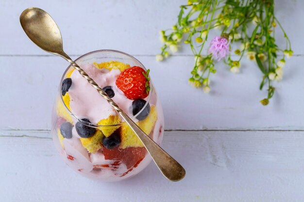 Foto bagatela de bayas con bizcocho y yogur en vaso con cuchara.