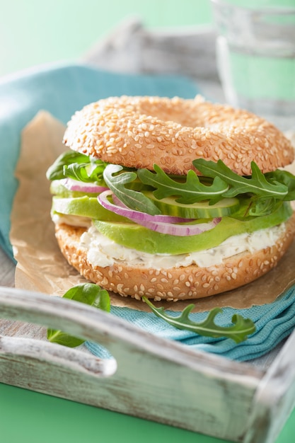 Bagel de aguacate con queso crema, cebolla, pepino y rúcula