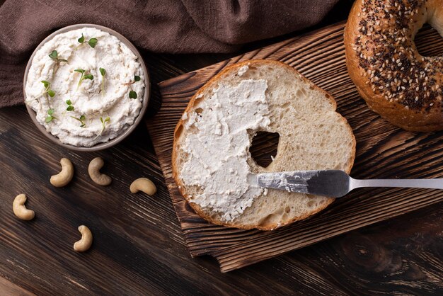 Bagel con queso crema de anacardos y nueces sobre fondo de madera oscura.