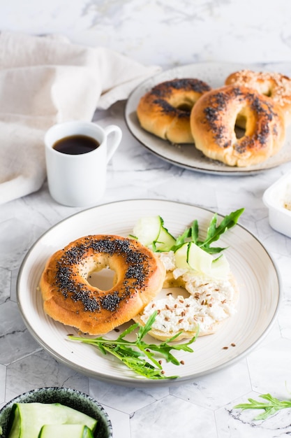 Bagel-Sandwich mit Frischkäse, Gurke und Rucola auf einem Teller Hausgemachtes Frühstück Vertikale Ansicht