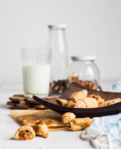 Bagels galletas de pastelería rellena con leche condensada en una placa de madera, un vaso de leche, postre en blanco