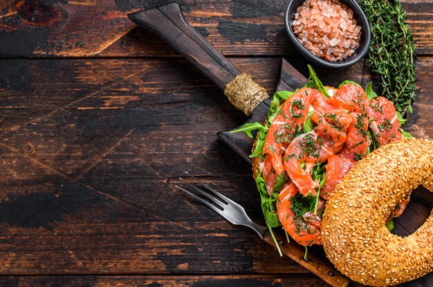 Bagelsandwich mit Lachs und Rucola. Dunkler Holztisch. Draufsicht.