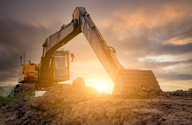 Bagger auf der Baustelle nach dem Graben des Bodens geparkt. Bulldozer auf Sonnenunterganghimmel und Wolkenhintergrund. Bagger nach der Arbeit. Erdbewegungsmaschine auf der Baustelle in der Abenddämmerung. Bagger mit Schmutzeimer.