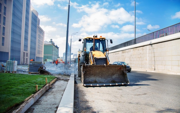 Bagger beim Straßenbau in der Stadt im Hintergrund des Geschäftsviertels