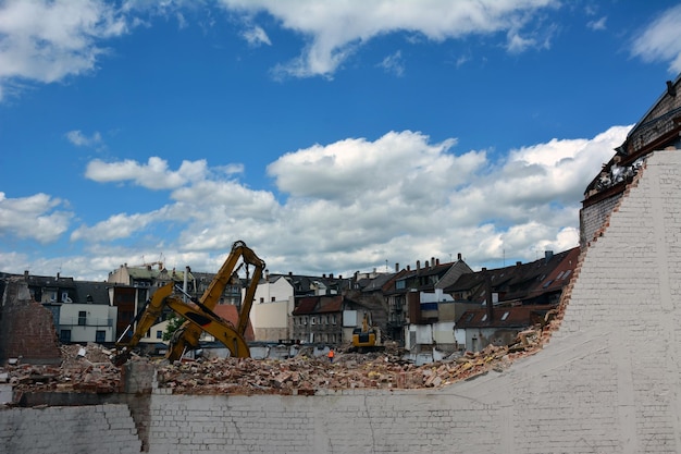 Bagger reißen ein Haus auf der Straße gegen einen hellen Himmel in einer antiken Stadt ab