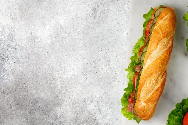 Baguete com presunto e legumes Sanduíche com presunto tomate alface pepino na placa de mármore Vista superior