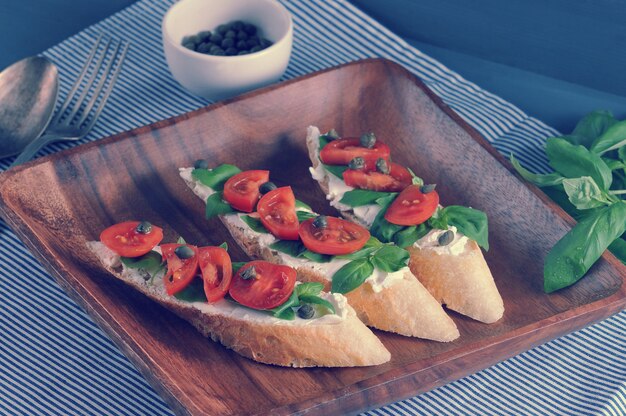 Baguete com queijo, manjericão, tomate cereja, alcaparras