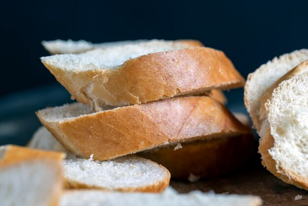 Baguete de trigo cortada em pedaços numa tábua de corte baguete de trigo branca cortada em fatias durante a cozedura