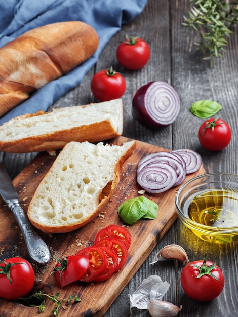 Baguete fresca cortada em pedaços, tomate, legumes e azeite, ingredientes para fazer um sanduíche vegano
