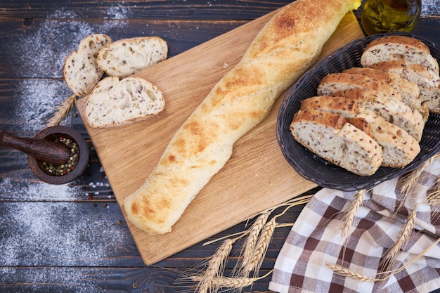 Baguete fresca e pão fatiado na tábua de madeira na mesa da cozinha