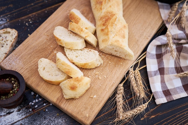 Baguete fresca e pão fatiado na tábua de madeira na mesa da cozinha