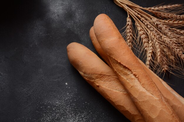 Foto baguetes francesas de pão fresco em um fundo escuro e trigo