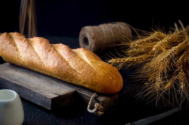 Baguette aus Weizenmehl auf altem Holzbrett mit Ährchen