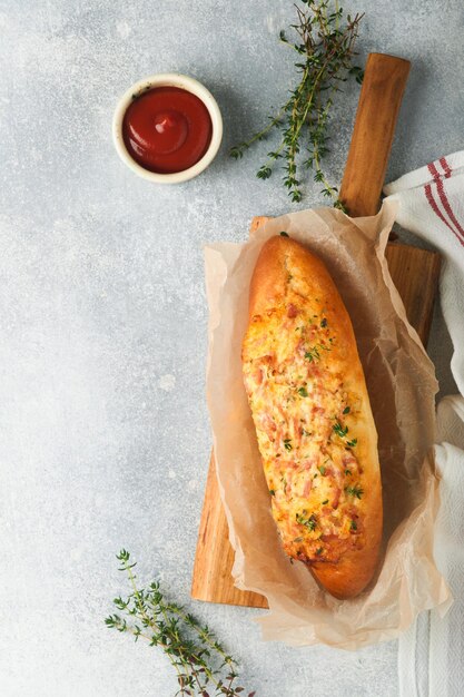 Baguette-Boote Heiß gebackenes Sandwich auf Baguette-Brot mit Schinken-Speck-Gemüse und Käse auf Pergament und Holzständer auf grauem Betongrund Draufsicht Kopierbereich