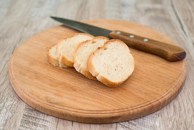 Baguette con un cuchillo y una tabla de cortar sobre una vieja mesa de madera.