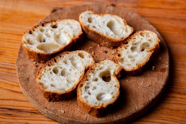 Baguette francesa en rodajas sobre una tabla de madera sobre un fondo claro Pan con agujeros grandes Preparándose para la bruschetta