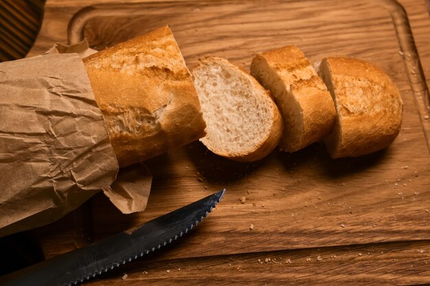Baguette fresca en un paquete artesanal parcialmente en rodajas y cuchillo de pan sobre tabla de cortar de madera
