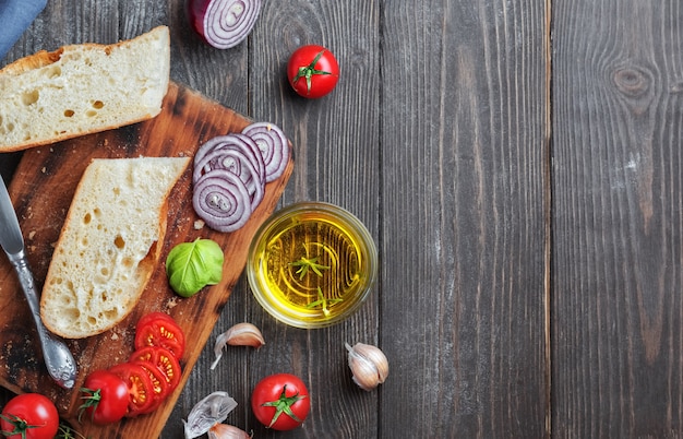 Baguette fresco cortado en trozos, tomates, verduras y aceite de oliva, ingredientes para hacer un sándwich vegano