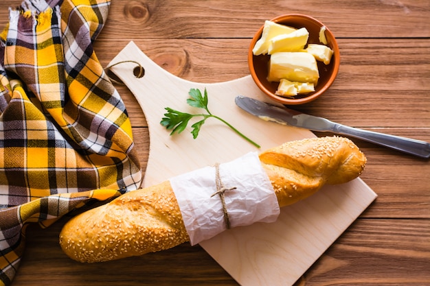 Baguette, mantequilla, cuchillo y perejil en una tabla de cortar. Vista superior