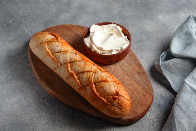 Baguette de pan de ajo en rodajas tostadas con requesón servido en tabla de cortar con servilleta de lino azul sobre concepto de panadería de fondo de piedra grisxA