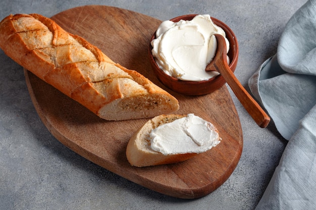 Baguette de pan de ajo en rodajas tostadas con requesón servido en tabla de cortar con servilleta de lino azul sobre concepto de panadería de fondo de piedra grisxA