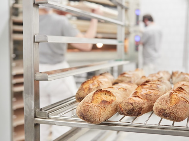 Baguette de pan en un carro de rejilla interior de una panadería trabajadores en el fondo desenfocado