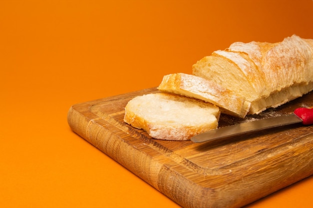 Baguette de pan en rodajas sobre una tabla de cortar de madera con un cuchillo sobre un fondo de color terracota