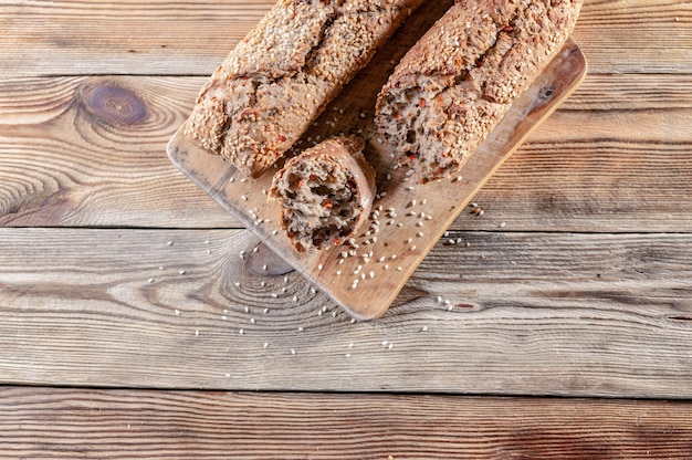 Baguettes apetitosos com sementes e porcas de sésamo em uma placa de corte em um fundo de madeira.