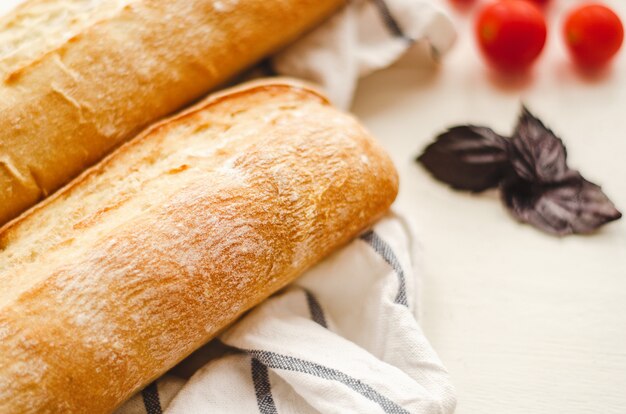 Baguettes frescos com uma batata frita em uma tabela branca em uma toalha com tomates e manjericão de cereja.