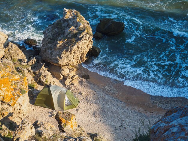 Bahía salvaje de mar con una carpa verde en la mañana al amanecer