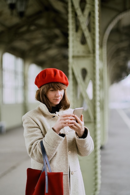 Bahnhof. Schönes Mädchen wartet auf Zug und schaut auf Handy. Frau reist leicht.