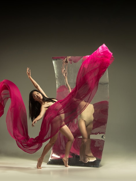Baila con fuego. Bailarina de ballet moderno en pared marrón con espejo. Reflejos de ilusión en la superficie. Magia de flexibilidad, movimiento con tela. Concepto de baile de arte creativo, acción, inspirador.