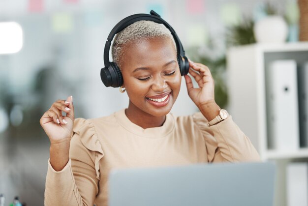 Baila a una mujer negra y feliz con música durante el descanso de la radio en el trabajo y escucha audio. Sonríe, alivia el estrés y baila. Empleado africano con auriculares para transmitir canciones de podcast y listas de reproducción.