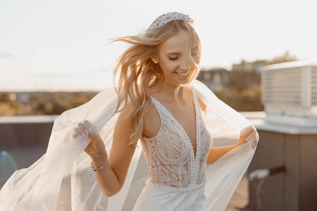 Bailando Hermosa novia sonriente, retrato de boda con peinado de novia, velo, vestido de novia. Feliz día en el techo. Estilo de vida, cabello al viento, felicidad.