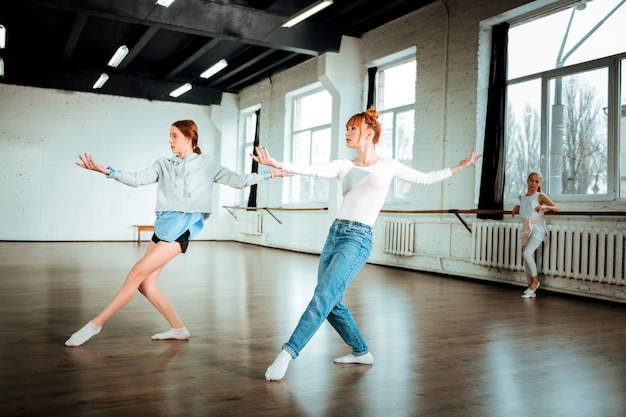 Bailando juntos. Hermosa bailarina profesional pelirroja vestida con jeans y su estudiante bailando en el estudio