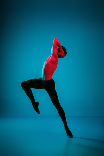 El bailarín de ballet atlético masculino que realiza la danza sobre fondo azul vivo. Tiro del estudio. Ballet moderno, concepto contemporáneo. Hombre joven en forma. Modelo caucásico