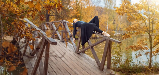 Bailarín de ballet moderno acostado en la barandilla del puente de madera en el parque de otoño Libertad armonía y unidad con la naturaleza