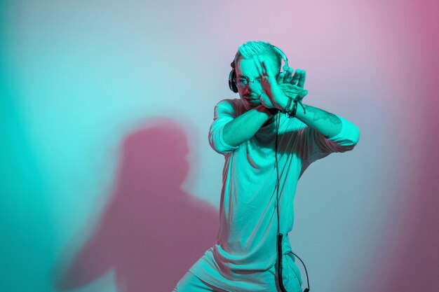 Bailarín hipster escuchando música con auriculares y bailando en el estudio con luz rosa y azul