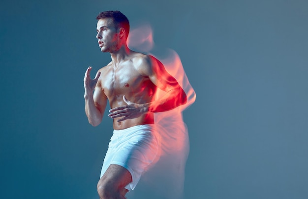 Bailarín masculino deportivo saludable en el entrenamiento de fitness de zumba en efecto de pintura de luz de estudio en azul