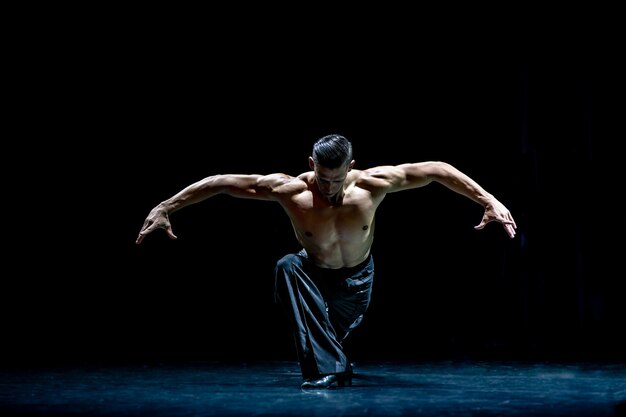 Bailarín de salón de baile muscular en topless haciendo pose aislado sobre fondo negro.